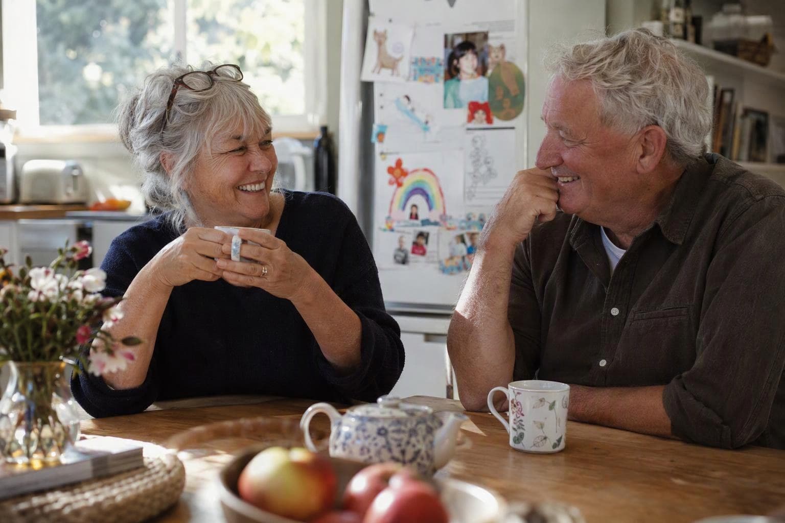 Two grandparents sharing a laugh over tea at the kitchen table